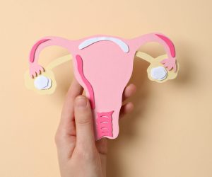 Paper uterus in female hand on beige background, top view