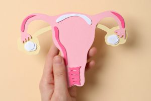 Paper uterus in female hand on beige background, top view